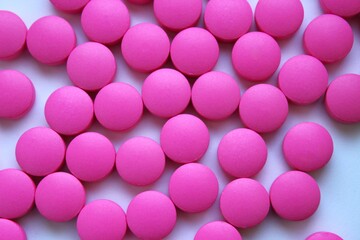 Macro close-up view of numerous pink round tablets arranged closely together on a flat surface. Simple pharmaceutical theme illustrating medication, supplements, or vitamins. 