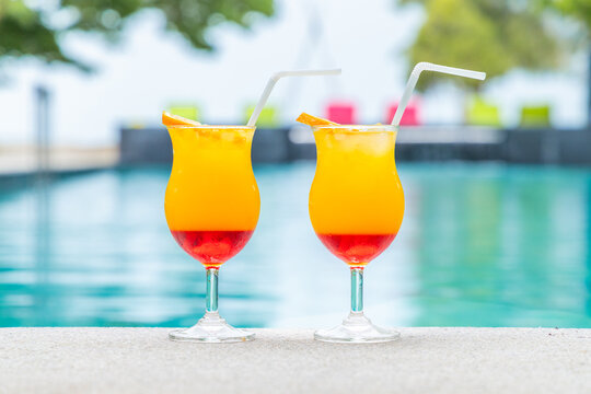Tropical cocktails by poolside, vibrant color drinks with straws, summer vacation relaxation, refreshing beverages, outdoor leisure setting.