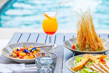 Vibrant poolside meal with gourmet dishes, tropical cocktail, summer outdoor dining concept.