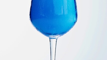 A tall glass filled with vibrant blue liquid against a white background