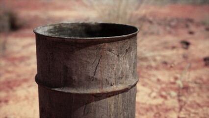 Naklejka premium A weathered metal drum stands solitary on the dry, cracked ground. Sunlight highlights its rustic charm in a stark landscape, evoking a sense of isolation and endurance of nature.