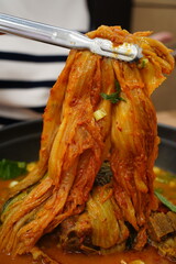 Tongs Lifting Spicy Korean Aged Kimchi from a Hot Pot