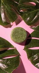 Natural Green Soap Bar Surrounded by Lush Tropical Leaves on Pink Background.