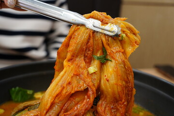 Tongs Lifting Spicy Korean Aged Kimchi from a Hot Pot