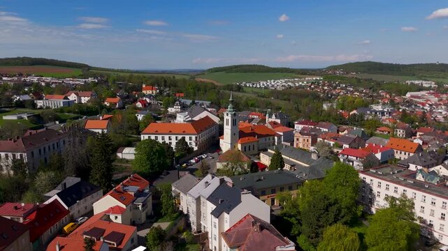 Cinematic aerial orbit around the historic Church of St. Bartholomew in Kutna Hora, Czechia, showcasing the iconic white tower and red roof under a bright blue sky.