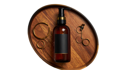 Overhead shot of a dark bottle, jewelry, on a wooden tray, against a black background