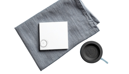 Still life features a white square, gray cloth, and black round object with blue cord, all on a flat surface
