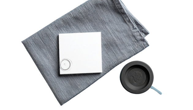 Still life features a white square, gray cloth, and black round object with blue cord, all on a flat surface