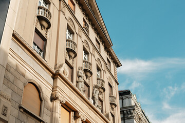 Fototapeta premium Elegant facade of classic architecture with balconies and sculptures under blue sky in Belgrade, Serbia country