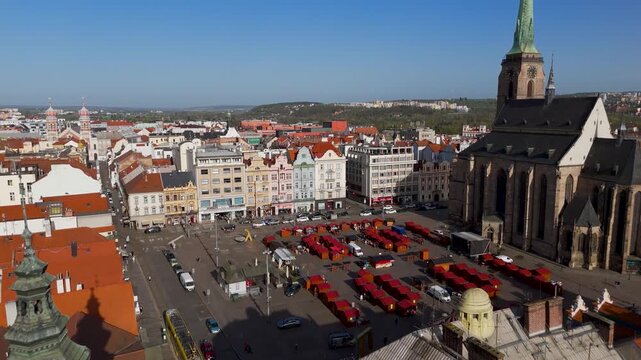 Aerial drone view flying low over the bustling Republic Square market in Pilsen, Czechia, highlighting the Gothic architecture of the Cathedral of St. Bartholomew on a bright sunny spring day.