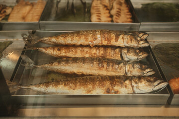Grilled whole fish arranged on metal tray in restaurant kitchen showcase