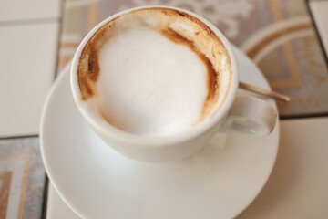 Closeup of hot cappuccino with thick milk foam on a white cup and saucer, perfect morning coffee mood