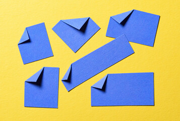 Blue paper message notes or sheets with folded edge dog-ear earmark and copy space for text on yellow background, top view flat lay conceptual desk backdrop