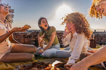 Friends enjoying pizza party on city rooftop at sunset