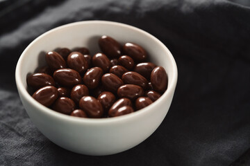 Milk chocolate dragee in white bowl on linen background