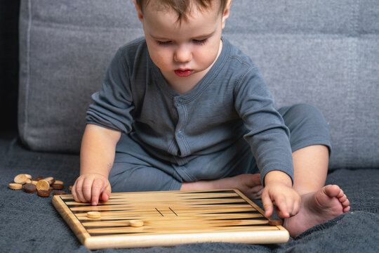 Curious toddler playing with wooden backgammon board at home.