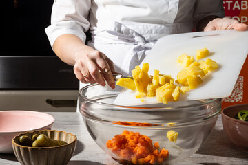Chef in a white apron dices boiled potatoes on a cutting board, transferring them into a glass...