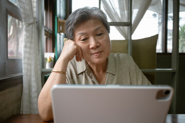 Asian Elderly Woman Actively Engaged using tablet, Various Online Activities from the Comfort of Her Home