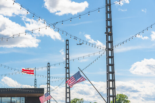 Airplane flies over American flags and string lights
