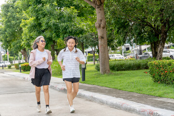 Obraz premium Two Asian senior women exercise with jogging along the road in the garden with day light.