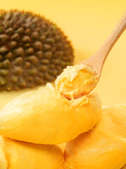 Close-Up of Creamy Ripe Durian Flesh on a Wooden Spoon with Bright Yellow Background