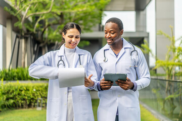 Two doctors man and woman walking and share a friendly conversation on the rooftop of a hospital during their lunch break. They discuss work and patient care while enjoying a sunny day in the city