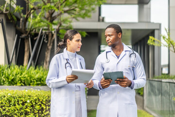 Two doctors man and woman walking and share a friendly conversation on the rooftop of a hospital during their lunch break. They discuss work and patient care while enjoying a sunny day in the city