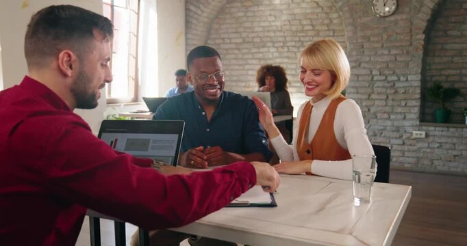 Happy multi-ethnic married couple, a Caucasian wife and an African American husband, sign a loan agreement with a bank officer in a modern banking office.