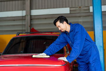 A professional Japanese man mechanic smiles and polishing a red classic car in a clean garage. guarantee of excellent cleaning and polish