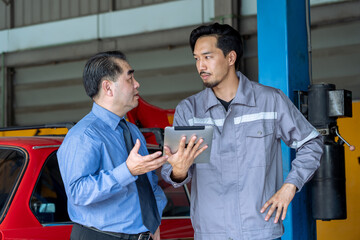 A professional Japanese mechanic uses a digital tablet to explain technical data to a senior manager in a garage car service . diagnostic report to a business-suited car owner in auto repair shop