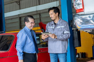 happy Japanese mechanic uses a digital tablet to explain technical data to a senior manager in a garage car service . diagnostic report to a business-suited car owner in auto repair shop