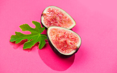 Fig fruits. Ripe sweet halved fresh figs fruit with leaf close-up, on pink background, flat lay, top view 