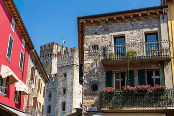 Picturesque streets of Sirmione, enjoying views of a historic Scaligero Castle and vibrant buildings under a clear blue sky by Lake Garda. Sirmione, Lombardy, Italy