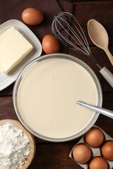 Liquid dough in bowl and ingredients on wooden table, flat lay