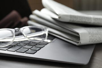Newspapers, laptop and glasses on grey table, closeup