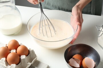 Woman making batter (liquid dough) at white table indoors, closeup