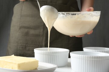 Woman pouring batter (liquid dough) into baking dishes at table indoors, closeup