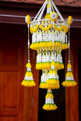 A beautiful Thai-style flower chandelier made from white and yellow flowers hanging from a wooden roof. Traditional Lanna decoration used in ceremonies and temple festivals in Thailand.