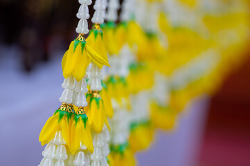 A beautiful Thai-style flower chandelier made from white and yellow flowers hanging from a wooden roof. Traditional Lanna decoration used in ceremonies and temple festivals in Thailand.