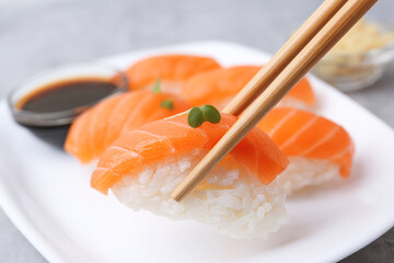 Taking tasty nigiri sushi with chopsticks at grey table, closeup