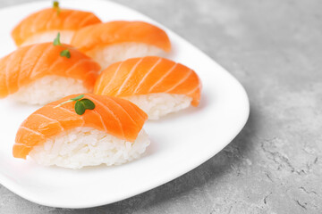 Delicious nigiri sushi with salmon and microgreens on grey textured table, closeup