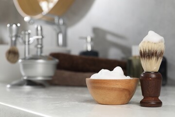 Shaving brush and foam on white textured counter indoors, closeup with space for text. Barber's tools