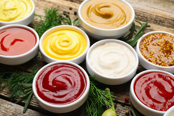 Different sauces in bowls and ingredients on wooden table, closeup