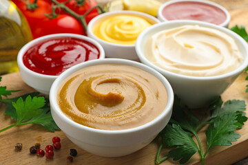 Different sauces in bowls and ingredients on wooden table, closeup
