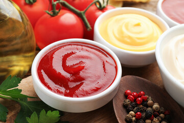 Different sauces in bowls and ingredients on wooden table, closeup