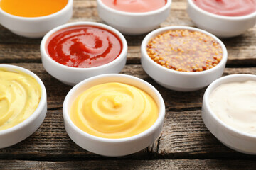 Different sauces in bowls on wooden table, closeup