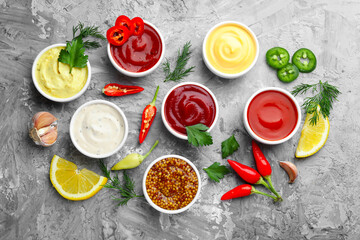 Different sauces in bowls and ingredients on grey textured table, flat lay