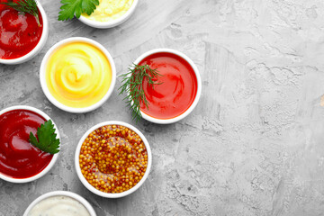 Different sauces in bowls and herbs on grey textured table, flat lay. Space for text
