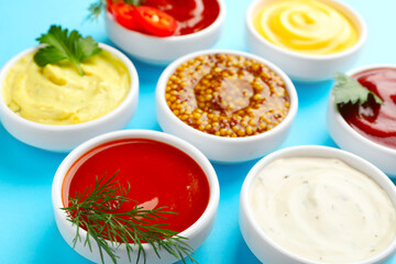 Different sauces in bowls and herbs on light blue table, closeup