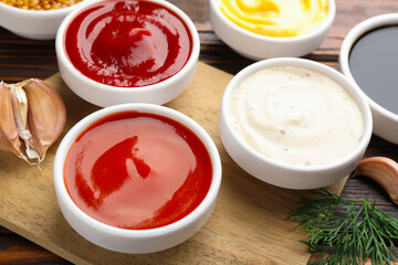 Different sauces in bowls and ingredients on wooden table, closeup